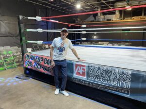Adrianos Facchetti standing beside a boxing ring with a banner promoting his Burbank fatal car accident lawyer services.